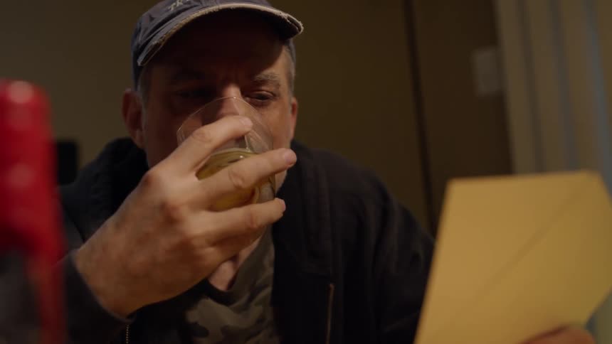A man drinks from a glass as he looks at a photograph