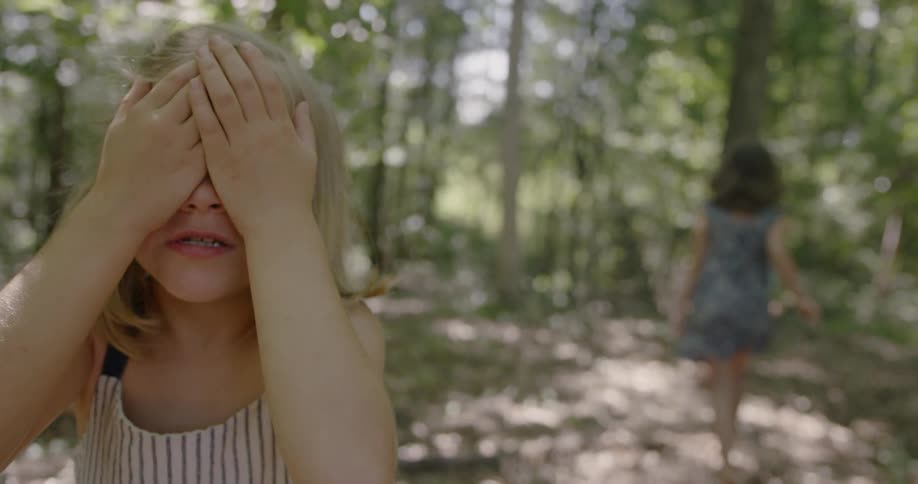 Child with hands over her eyes as child behind her run away