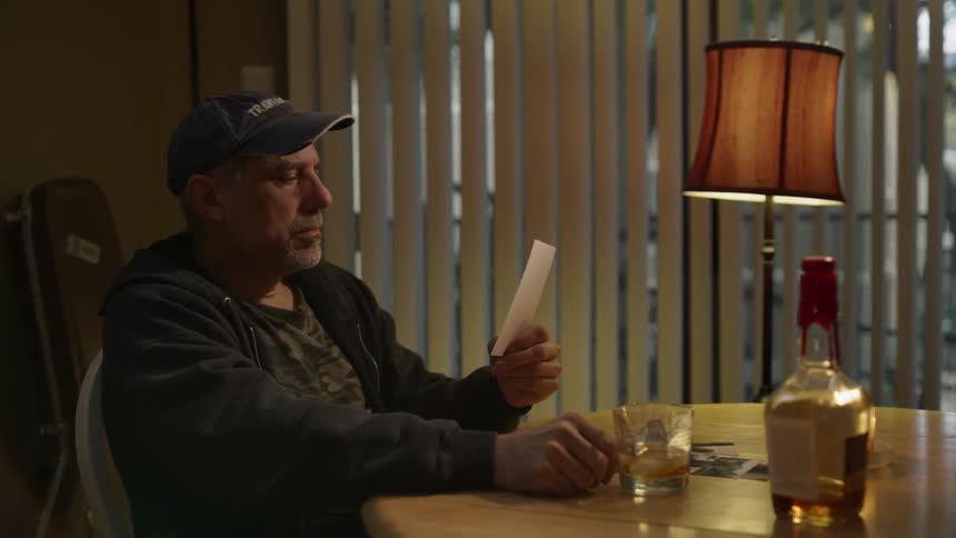 A man looks at photographs while drinking whiskey
