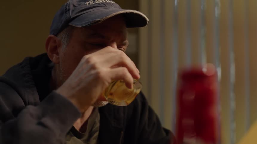 A man is taking a drink of alcohol as he sits at a table looking at old photos at night