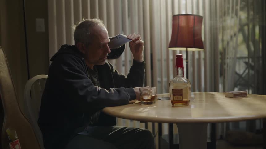 A man lifts his hat off in front of a drink at a table