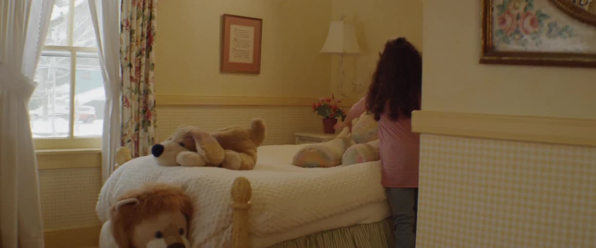 A girl is removing a stuffed teddy bear from her bed during the day
