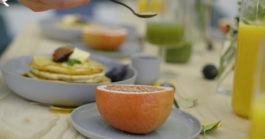 A woman sprinkles sugar on a cut grapefruit