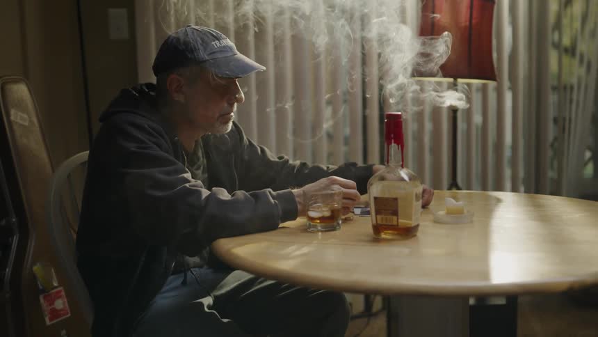 A man smokes and drinks alone at a table
