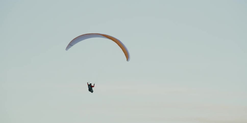 A person paraglides slowly over the mountain