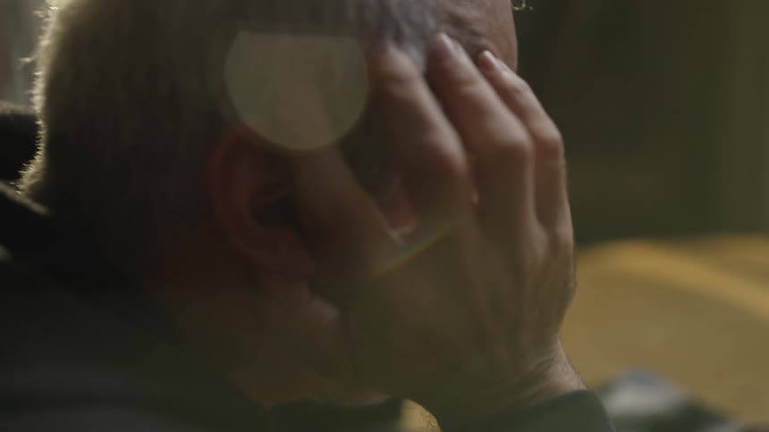Man rests his head in his hands while drinking whiskey