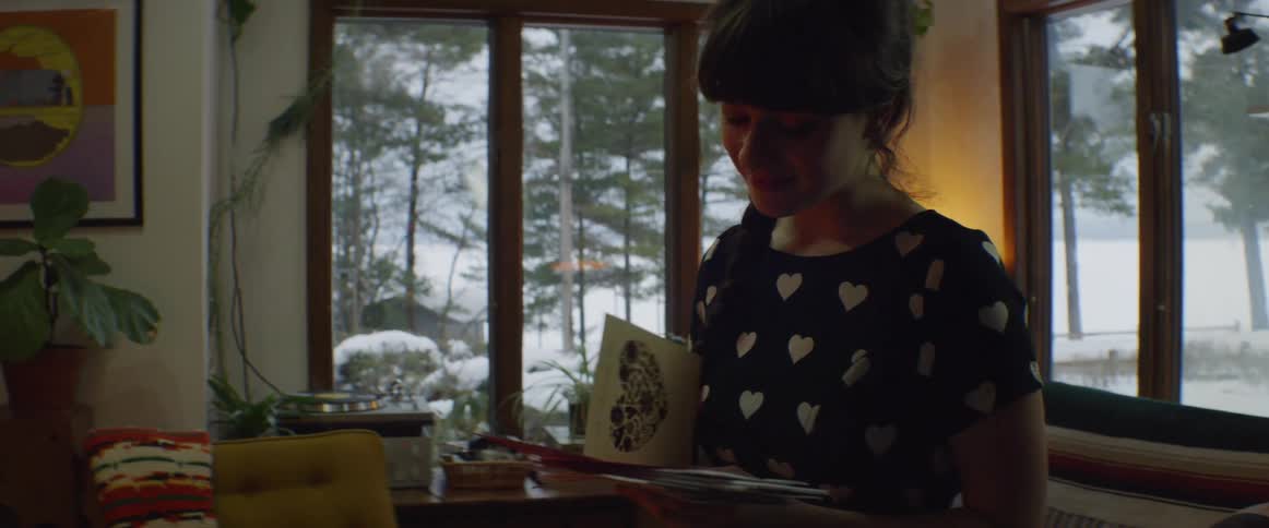Woman stands in house holding mail and reading a card