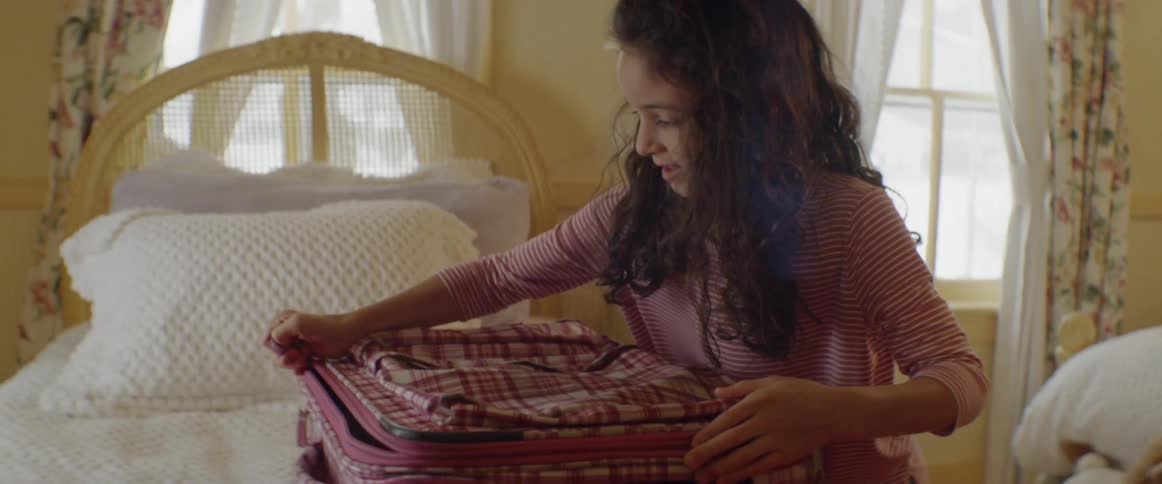 A child zips her luggage case shut