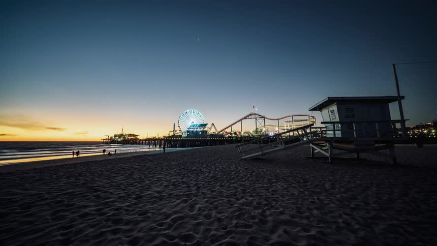 The sun sets behind a beach amusement park