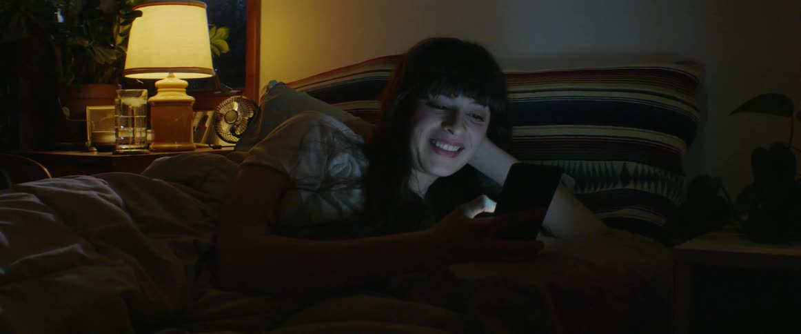 Woman smiles while scrolling on her phone in bed
