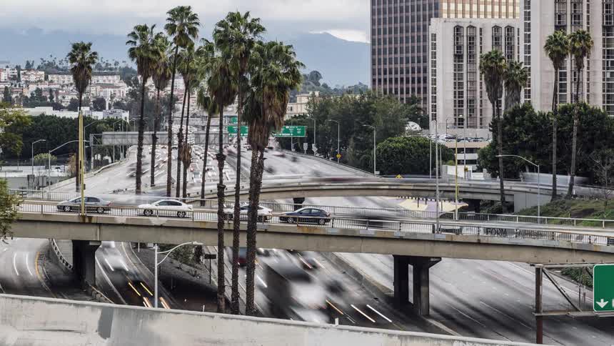 Cars travel fast over the highway past the buildings