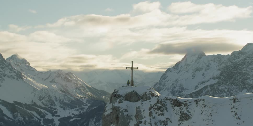 The person is standing near a cross on the mountain