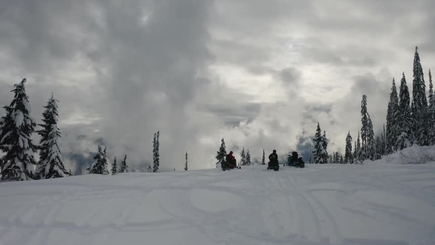 People on snowmobiles watch the heavy clouds ahead
