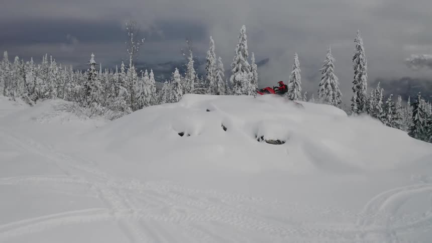 A person jumps over a hill on a snowmobile