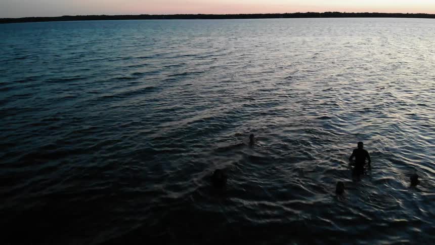 People wade and swim in the ocean at sunset