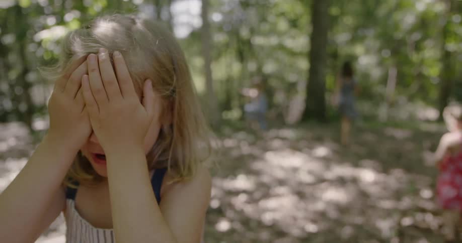 Child with hands over her eyes as child behind her run away