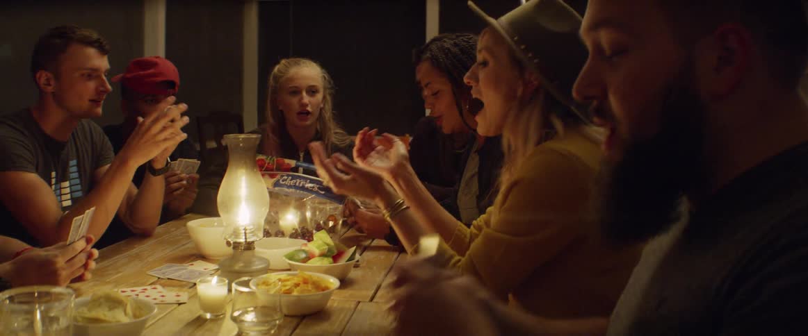 Men and women sit around a candle lit table playing cards