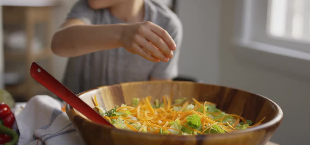 Child grabs carrots and puts them in a salad bowl