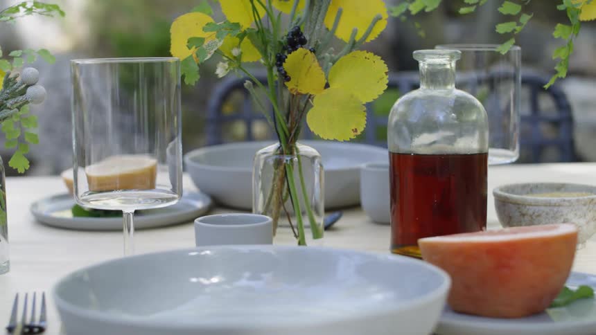 An outdoor table is set and decorated with vases of leaves