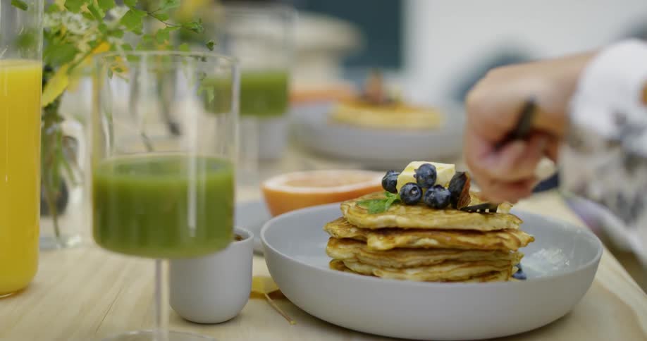 Person cuts into a stack of blueberry pancakes