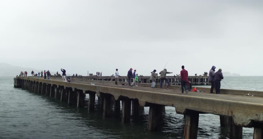 People walking on and fishing off of a pier on a cloudy day