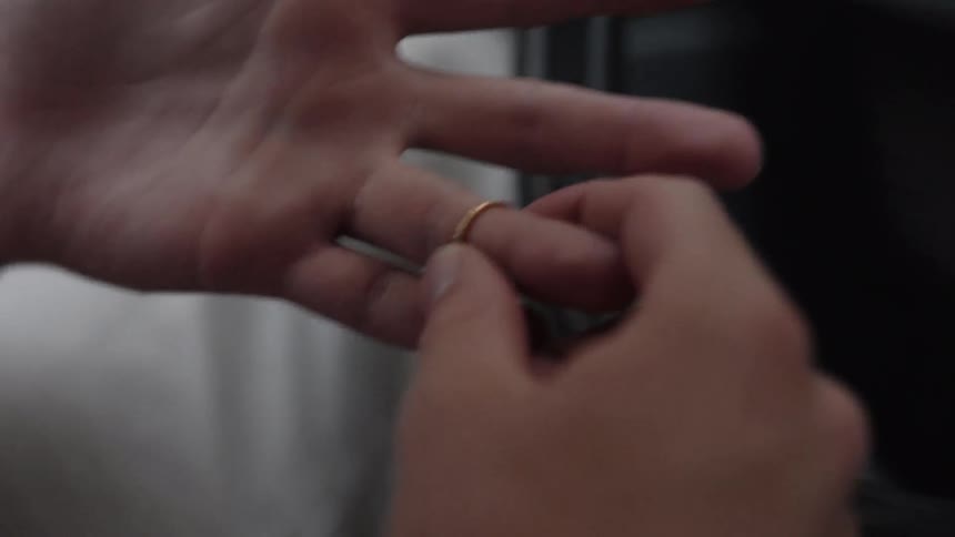 A man sitting in the driver's seat takes a gold ring off his finger