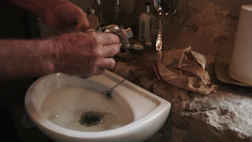 A man cleans a candle holder over the sink
