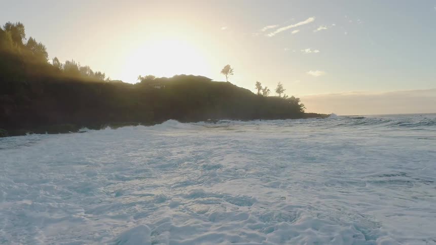 Foamy waves crash into shore under a sunny sky