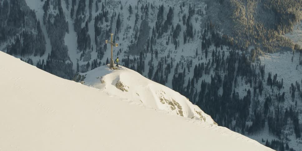 Man standing next to large cross statue on top of snow covered mountain
