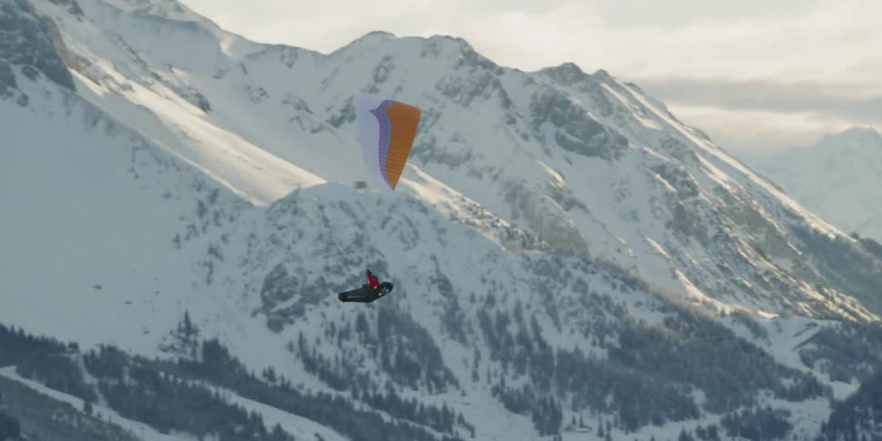 A person paraglides past the snow covered mountains