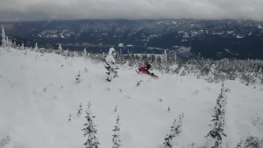 Person riding on a snowmobile over hills and through trees