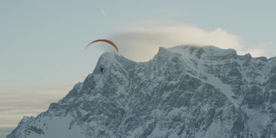 A person parasails towards the snow covered mountains