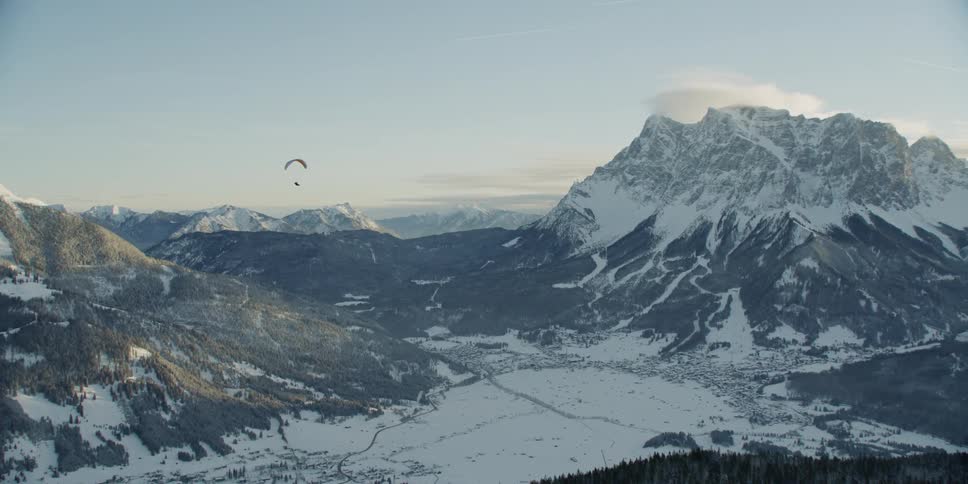 Person paragliding in a snowy valley area on a mostly clear day