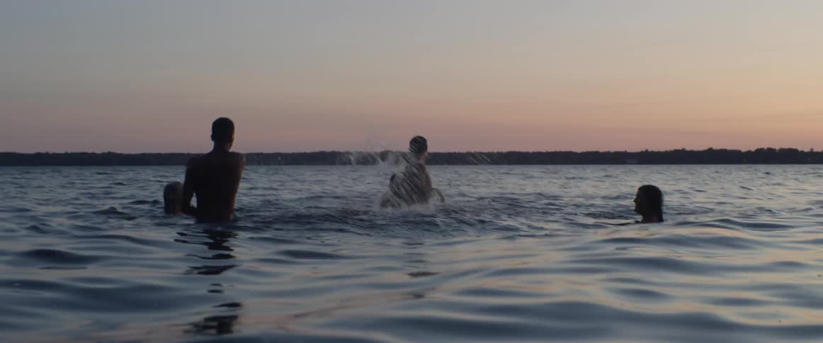 People swim in a lake at sunset
