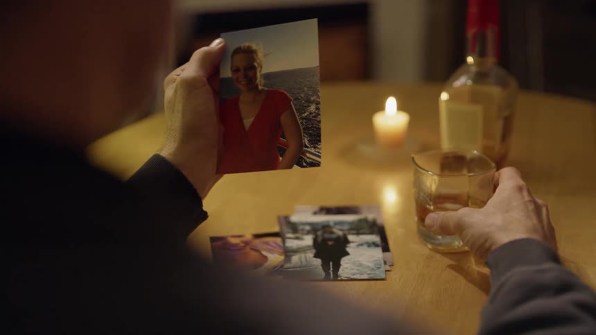 Man holds glass of whiskey and looks at picture of a woman