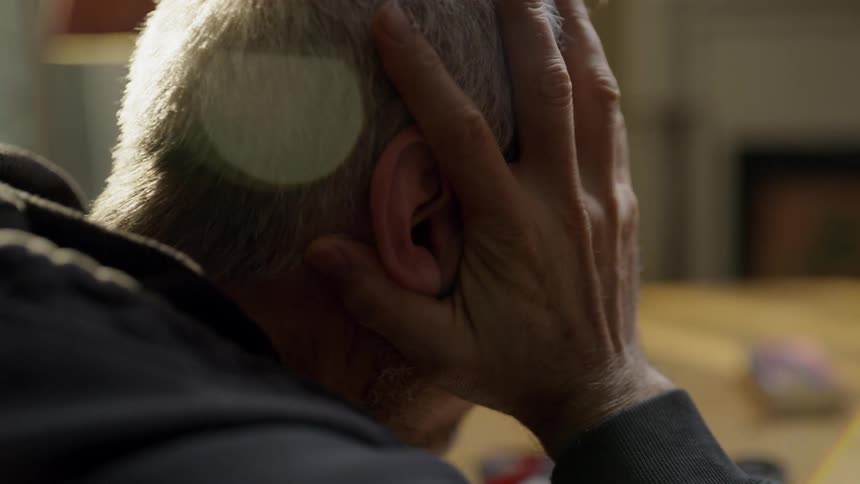 A man sits at the table rubbing his face