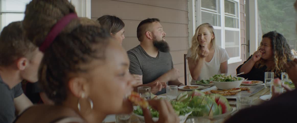 Group of people are talking and eating at table on porch