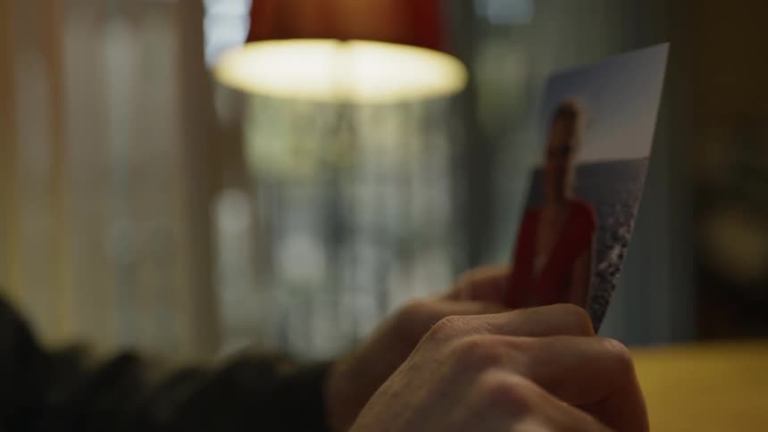 Man holds a photograph in his hand as he sits at a table