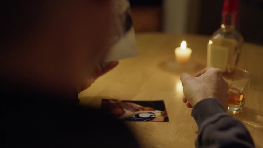 Man sits at table drinking whiskey and looking at pictures