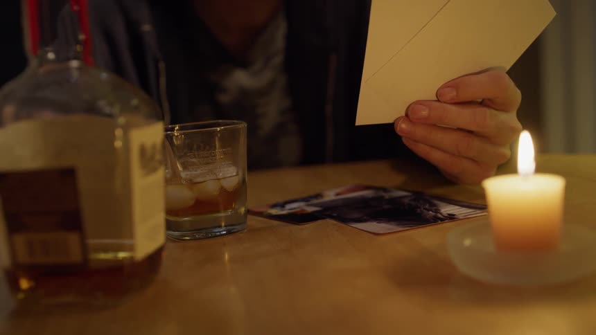 Man drinks whiskey while looking at photographs
