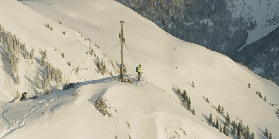 Man stands next to a large cross on a snowy mountain peak