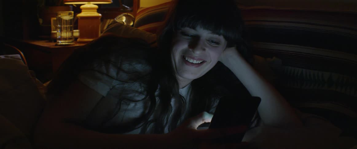 The woman laughs in bed while looking at her phone