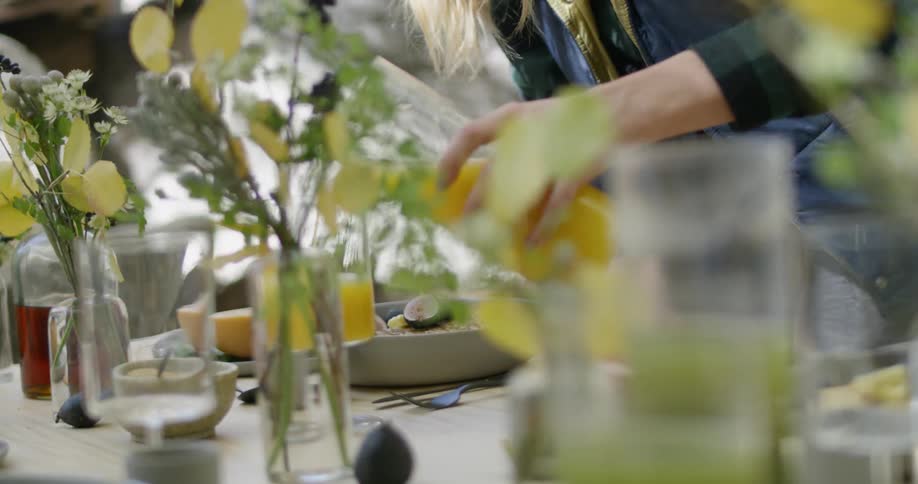 Person pours orange juice into a glass on a flower covered table outside