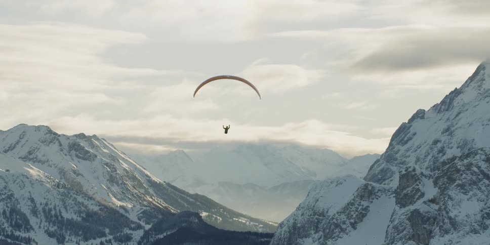 Person paragliding over snowy mountains