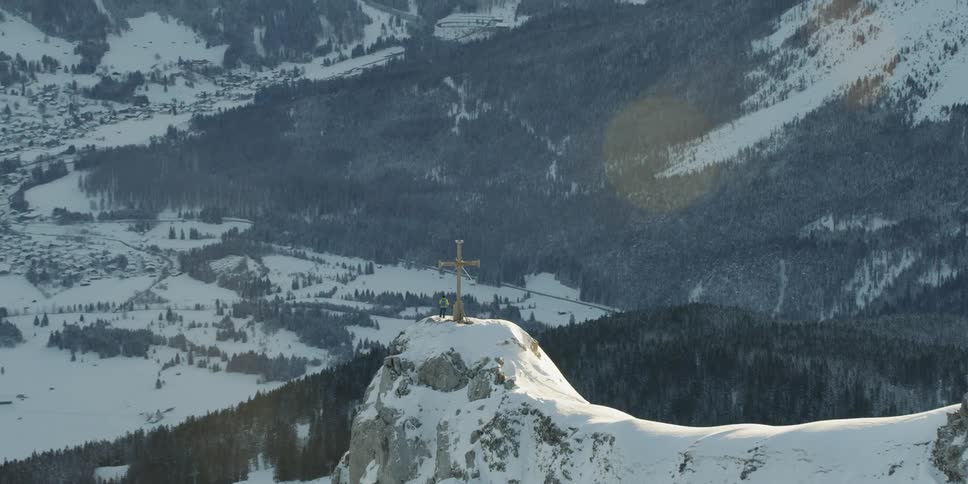 Man standing next to large cross statue on top of snow covered mountain