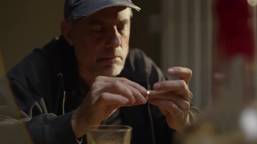A man is drinking and looking at wedding bands as he sits inside at a table