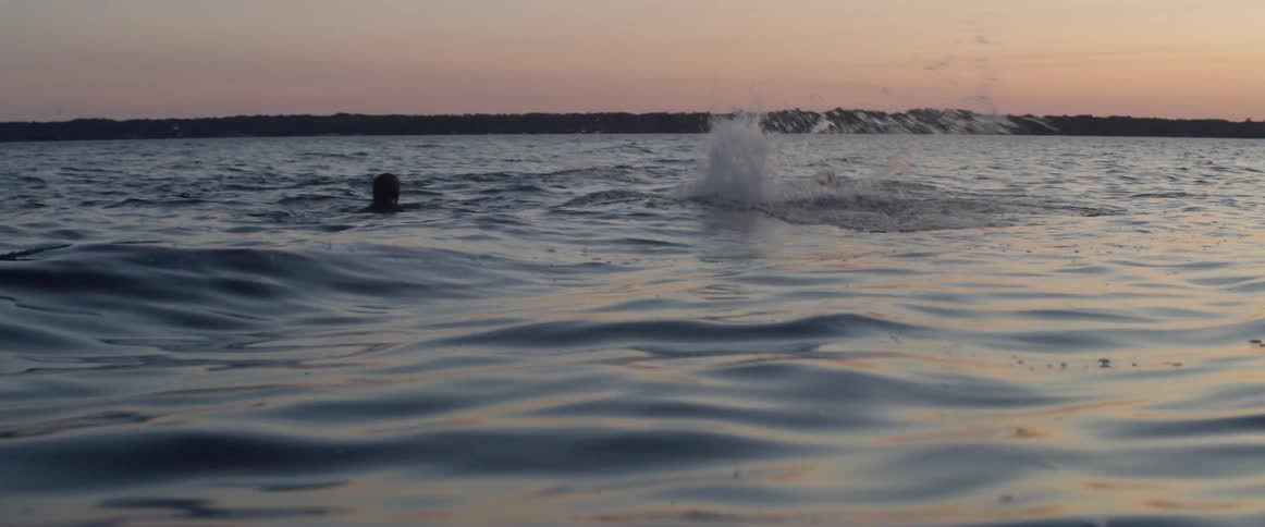 People swim in a lake at sunset