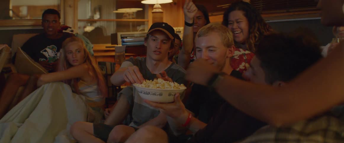 A person hands a bowl of popcorn to friends sitting on the floor