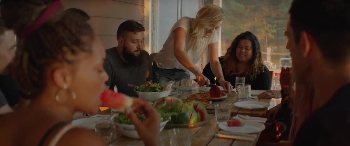 A woman slices pizza for a group of friends sitting around the table