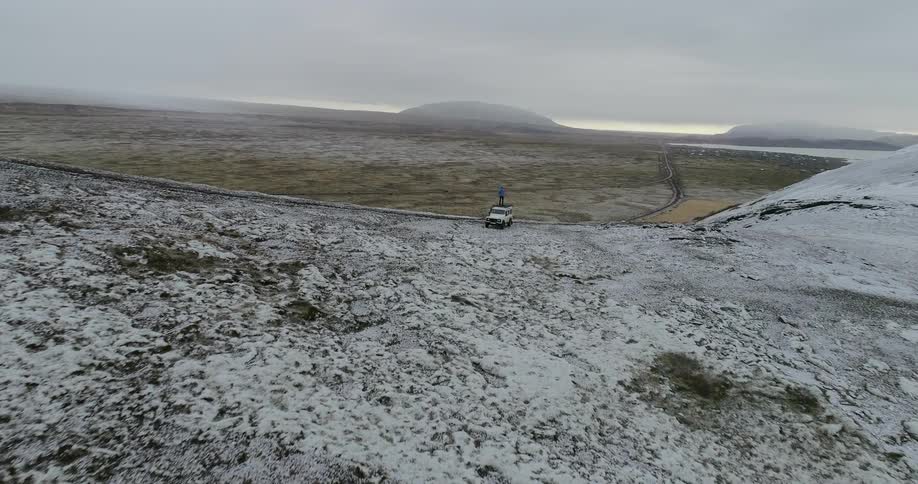 The hills are covered with snow and a person standing on a vehicle